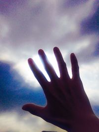Low angle view of cropped hand against cloudy sky