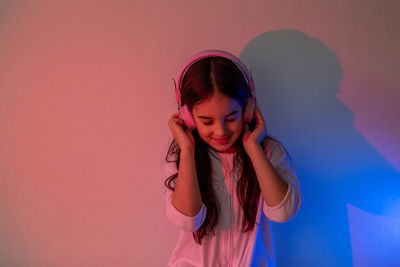 Beautiful happy little girl in headphones listening to music in neon light