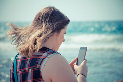 Midsection of woman using mobile phone against sea