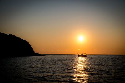 Silhouette boat sailing in sea against clear sky during sunset