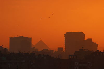 Pyramids and buildings in city against orange sky in egypt