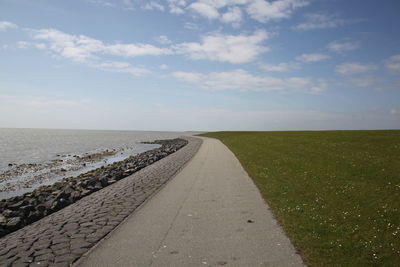 Empty footpath by sea against sky