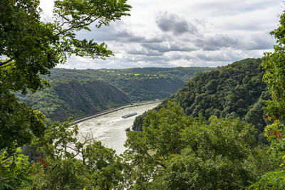 The river rhine in western germany flows between the hills covered with forest, visible barge.
