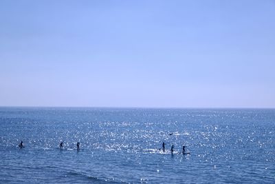 People in sea against clear blue sky