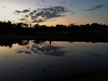 Reflection of silhouette trees on water against sky