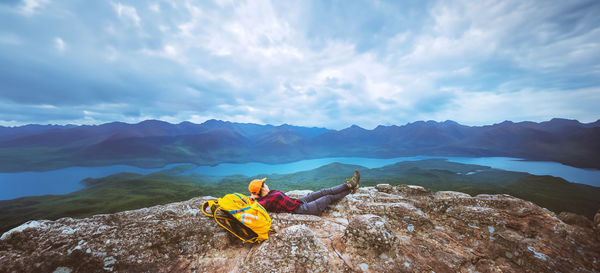 Rear view of woman sitting on rock against sky