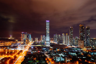 Illuminated cityscape against cloudy sky at night