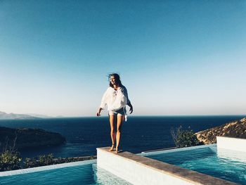 Full length of woman standing against sea at poolside on sunny day