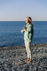 Young concentrated woman prepares to stand on sadhu nail board for practice by the sea.