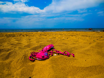 Pink bikini top on sandy beach against sky