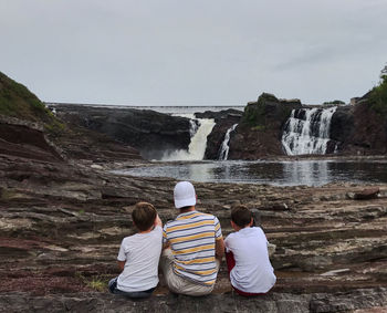 Rear view of people sitting on rock against sky