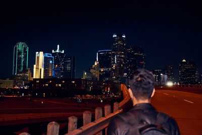 Rear view of man and illuminated buildings against sky at night