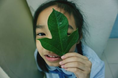 Close-up high angle portrait of girl covering eye with leaf