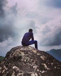 Man sitting on rock against mountain