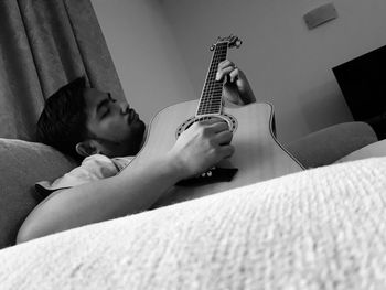 Young woman playing guitar on sofa at home