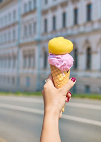 Ice cream cone in hand close-up with bokeh. gelato with peach sorbet and lavender flavor.