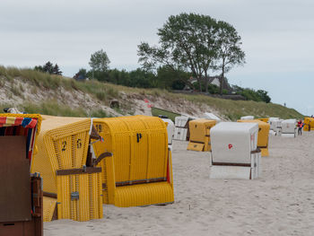 Hooded chairs on sand at beach against sky