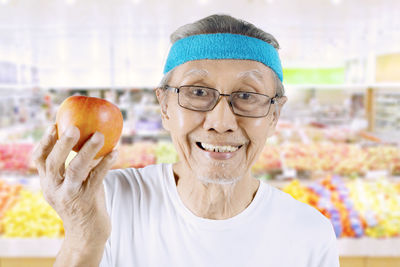 Portrait of senior man holding apple at market