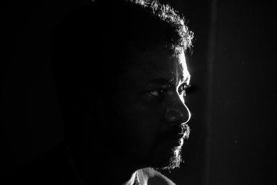 Close-up of young man looking away against black background