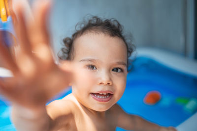 Happy kid playing in an inflatable pool in backyard. curly toddler smiling and playing with water