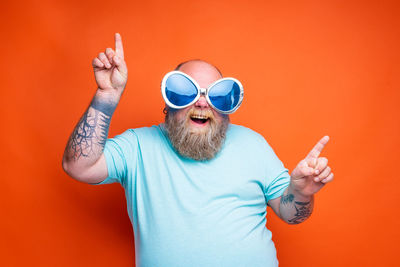 Man wearing sunglasses standing against orange background