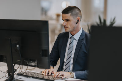 Confident young businessman typing while using computer at desk in office