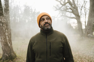 Smiling male explorer looking away while standing in forest