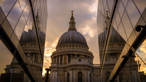Low angle view of st paul cathedral reflecting on modern buildings during sunset