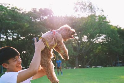 Side view of smiling young man playing with dog in park