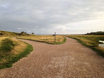 Empty road amidst field against sky