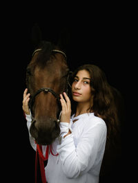 Portrait of young woman riding horse against black background