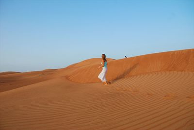 Woman walking on sand dune in desert against clear sky