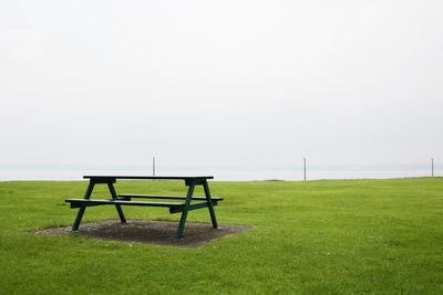 Empty bench on field against clear sky