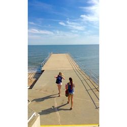 High angle view of female friends walking on pier against sky