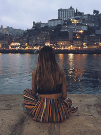 Rear view of woman sitting at promenade in city during dusk