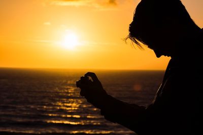 Silhouette woman photographing against sea during sunset