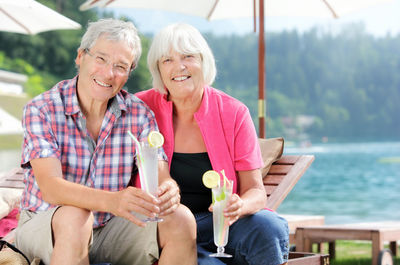 Portrait of senior couple sitting against lake