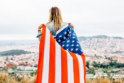 Rear view of man holding flag against sky