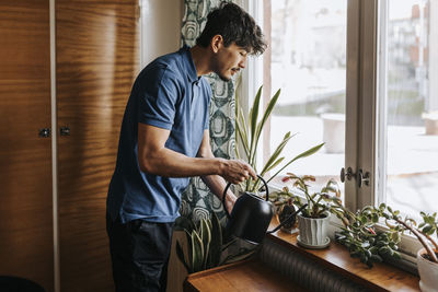 Male care assistant watering plants on window sill at home