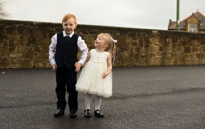 Happy well-dressed siblings holding hands while standing on road