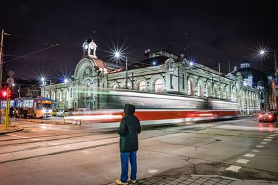 Rear view of a man walking on illuminated road in city