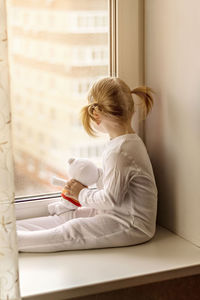 Full length of girl with stuffed toy sitting by window