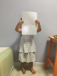 Girl covering face with drawing paper at home