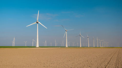 Windmills on field against clear blue sky