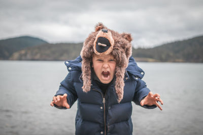 Portrait of boy screaming while standing against lake