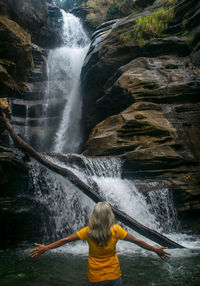Rear view of woman standing in waterfall
