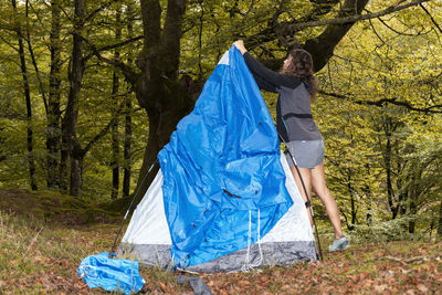 Young woman with outdoor gear setting up his tent in a clearing after a day of hiking in the woods