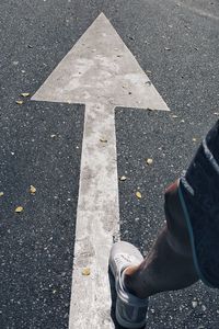 Low section of man standing on arrow road sign 