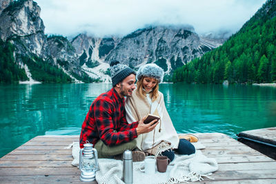 Young woman using smart phone by lake against mountains