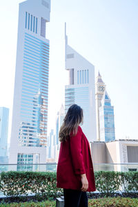 Woman standing by buildings in city against sky